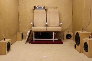 Image of an acoustic testing room featuring two airplane chairs and multiple speakers.
